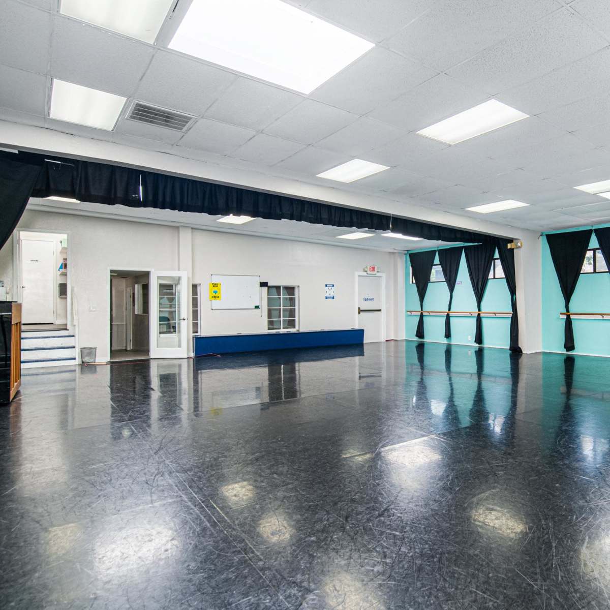 An empty dance studio with a black floor, light blue walls, and a row of mirrors along one side.