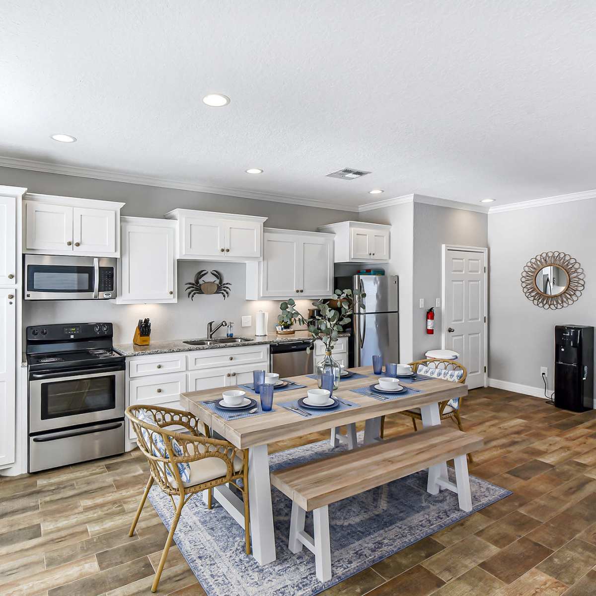A modern kitchen with white cabinetry, stainless steel appliances, and a wooden dining table set for four.