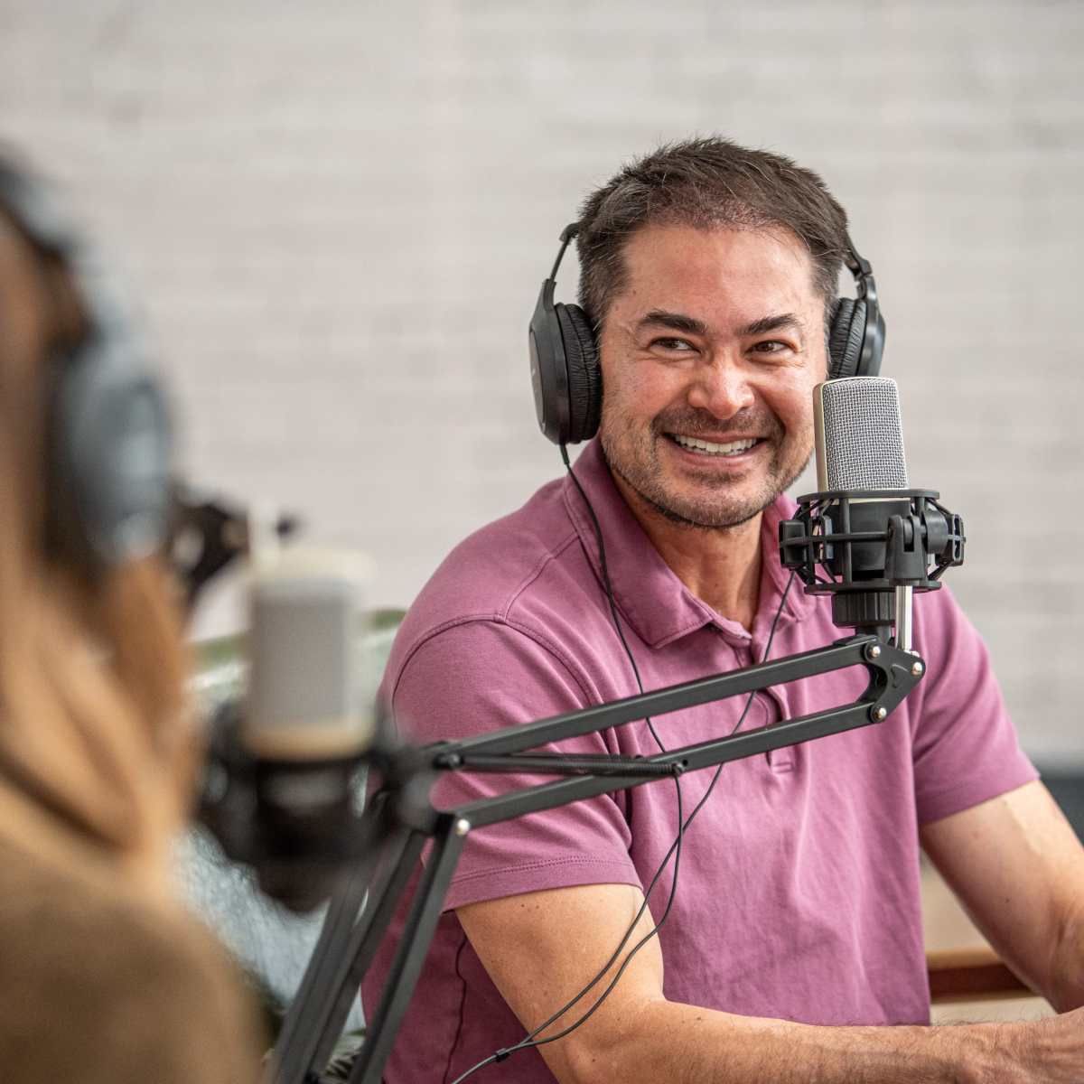 A man in a purple shirt smiles while speaking into a microphone during a podcast recording.
