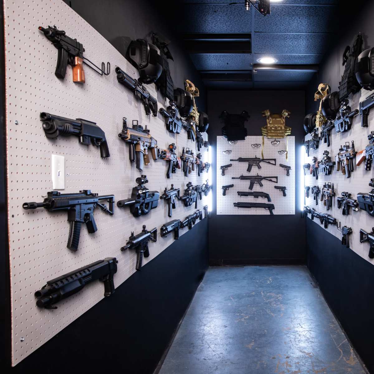 A narrow hallway with walls lined with various firearms displayed on pegboards.