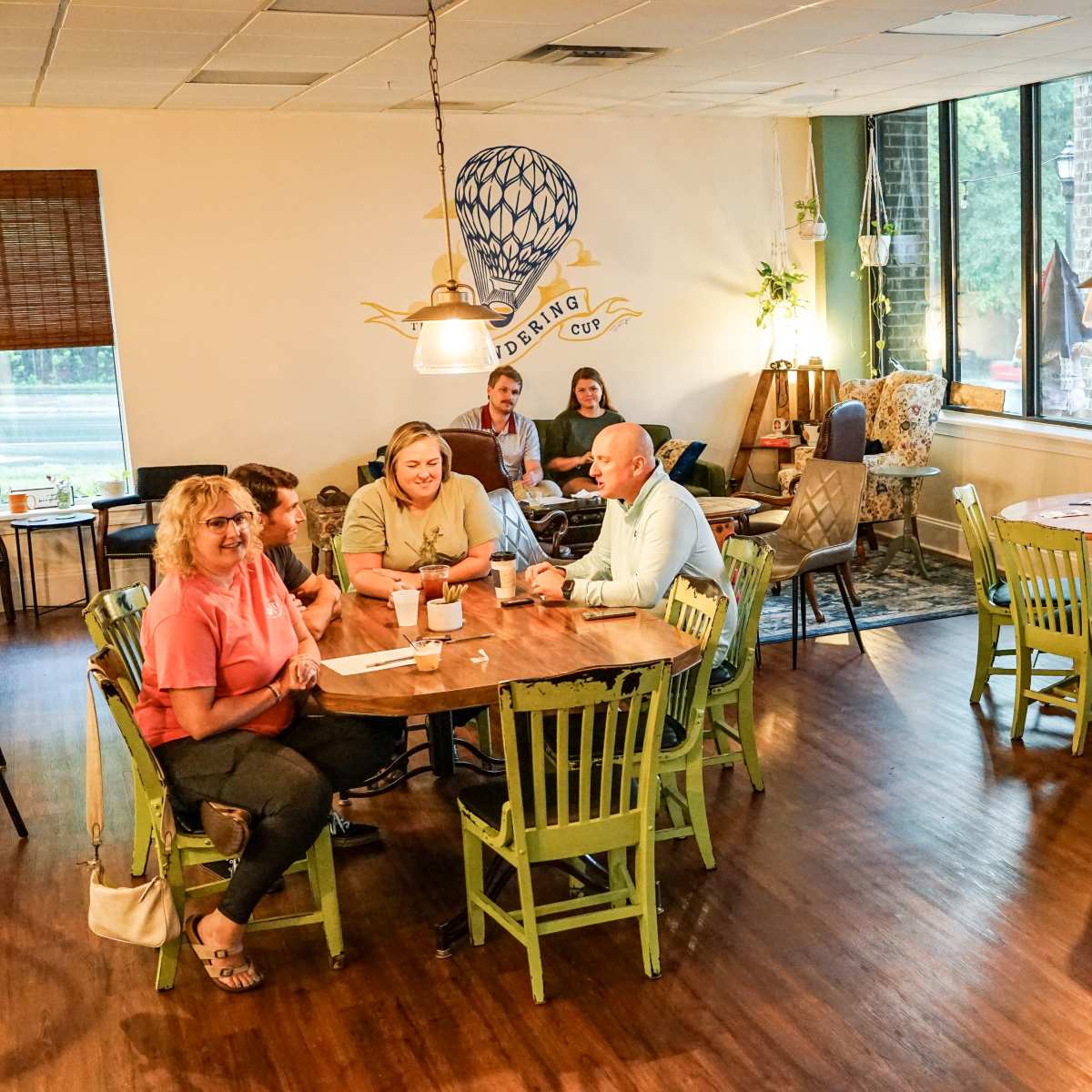A cozy café interior with groups of people sitting at wooden tables, enjoying drinks and conversations under warm lighting.