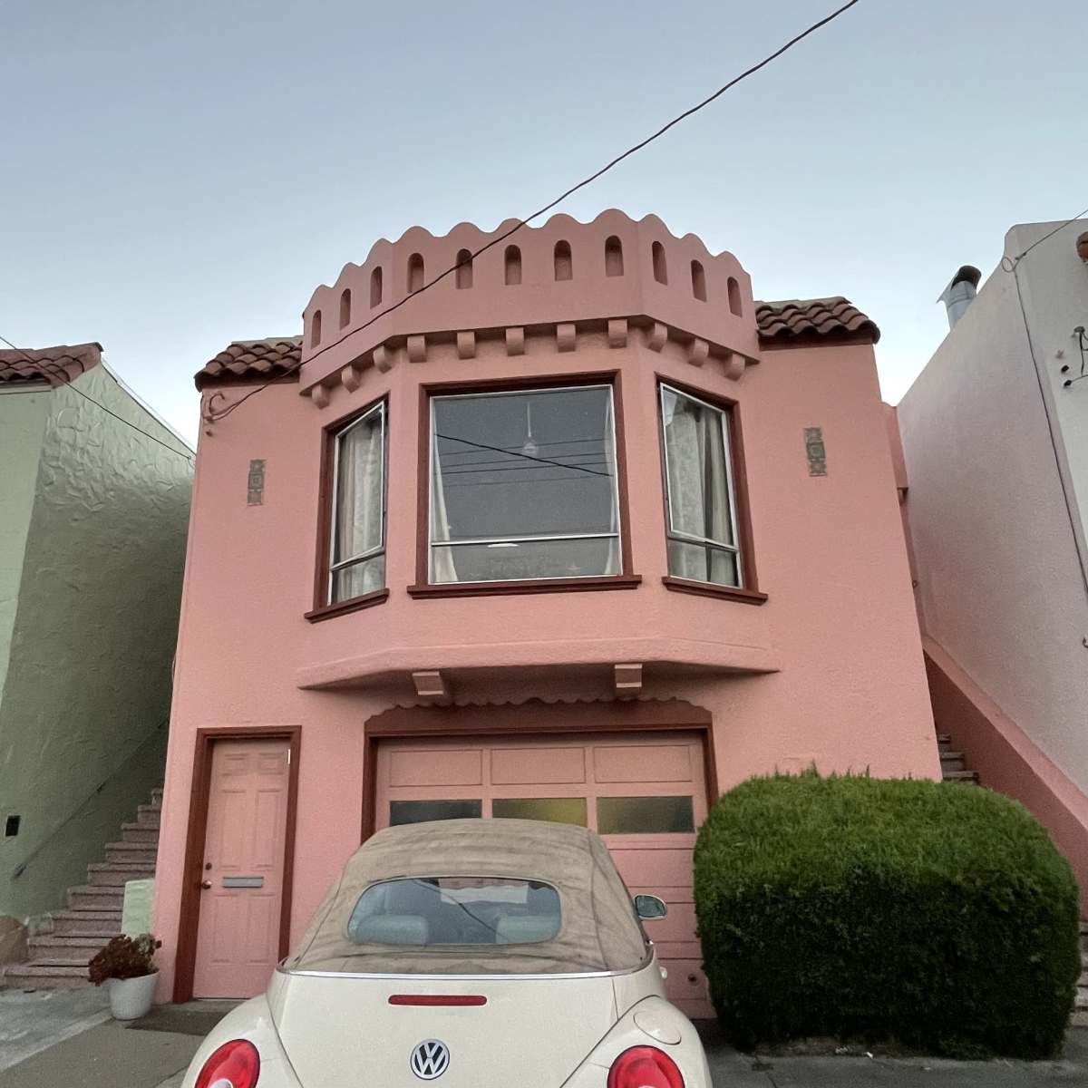 A pink house with a rounded turret and a large window is located above a car parked in front.
