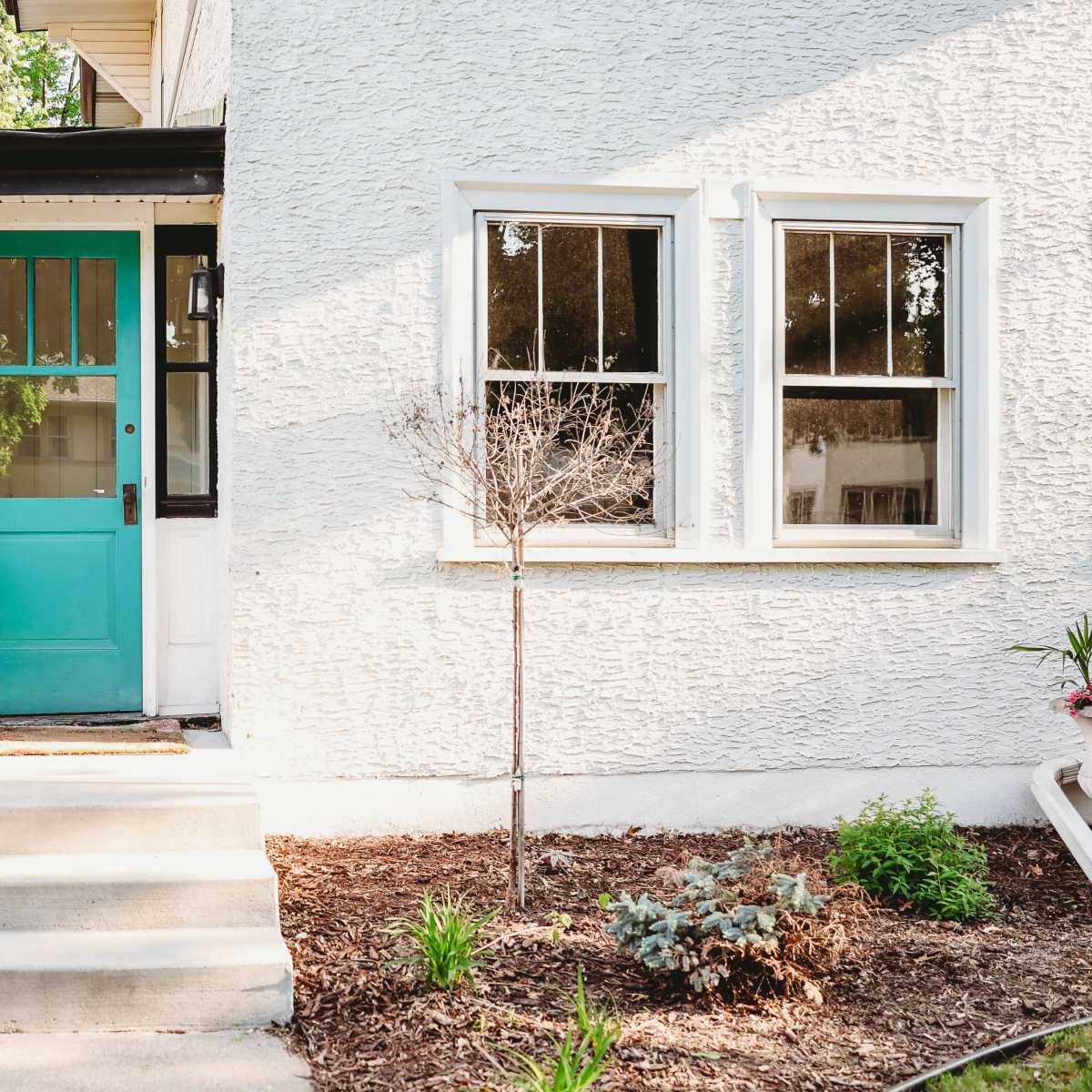 A house with a turquoise door and a small garden area featuring potted plants and mulch.