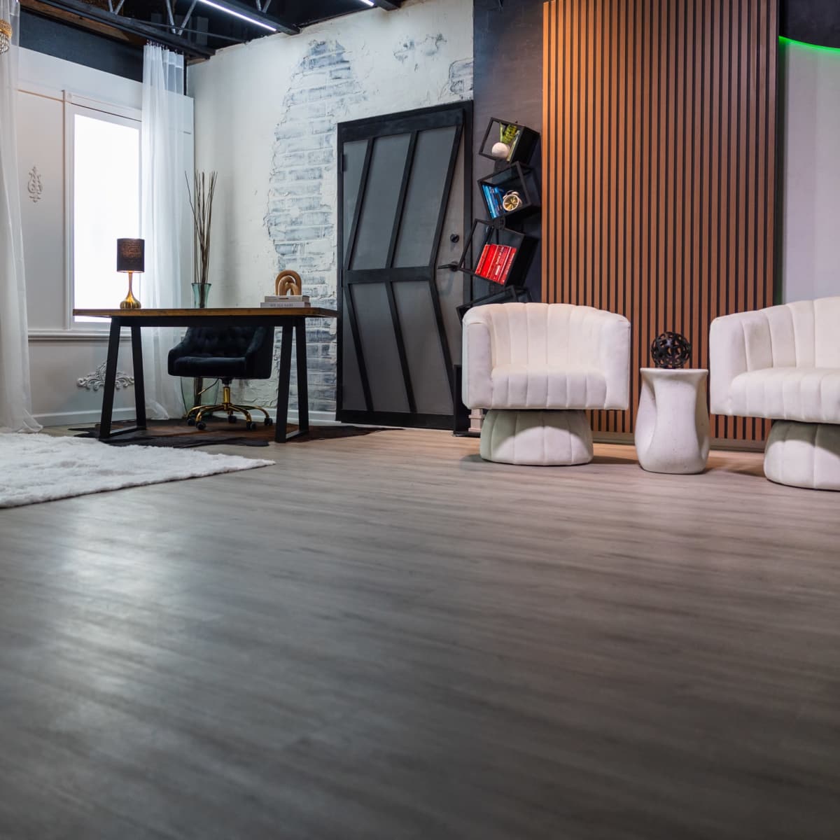 A modern interior space featuring a desk, two white chairs, a small chair, and decorative elements like a rug and a flower arrangement.