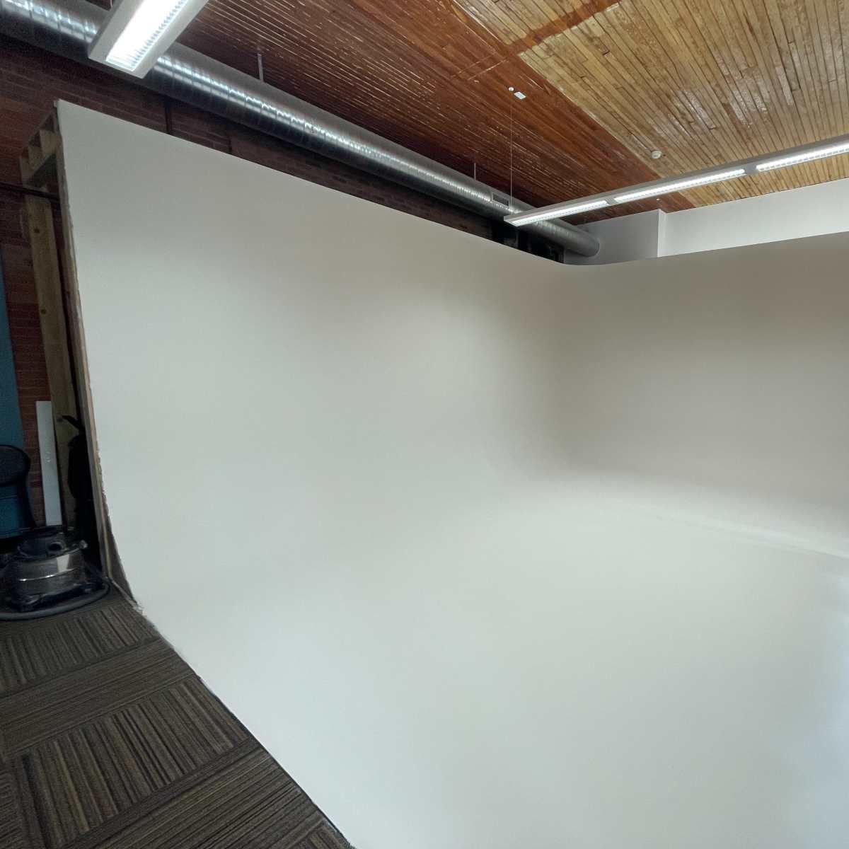 A spacious photography studio featuring a seamless white backdrop and a wooden ceiling.