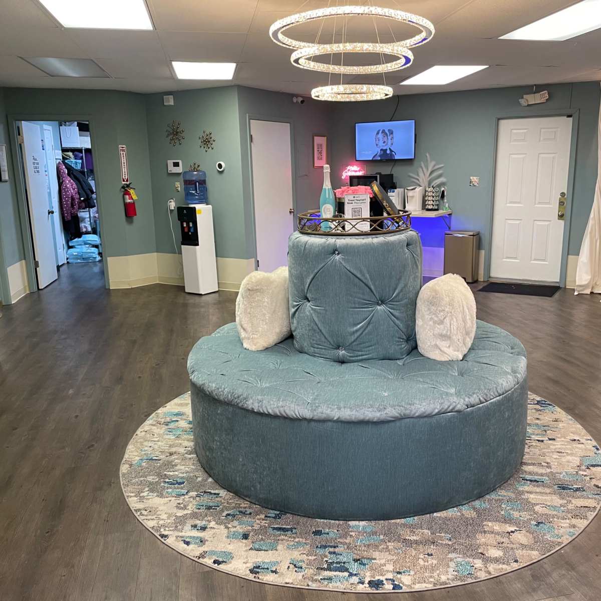 A modern waiting area with a circular tufted seating arrangement, surrounded by a patterned rug, and illuminated by overhead circular lights.