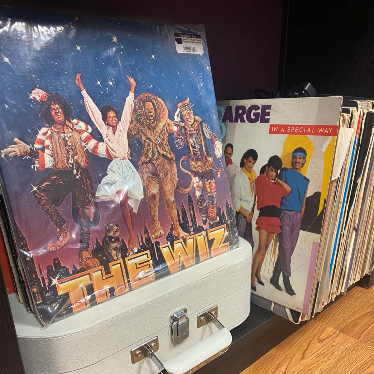 A collection of vinyl records, including "The Wiz," displayed alongside a white suitcase and various album covers.