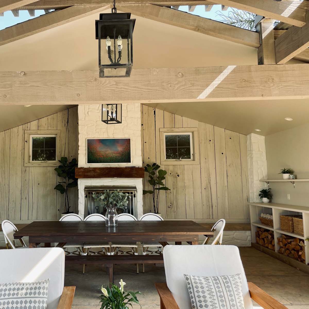 A spacious, well-lit indoor seating area with a long wooden dining table, surrounded by chairs and decorated with potted plants and artwork on the walls.