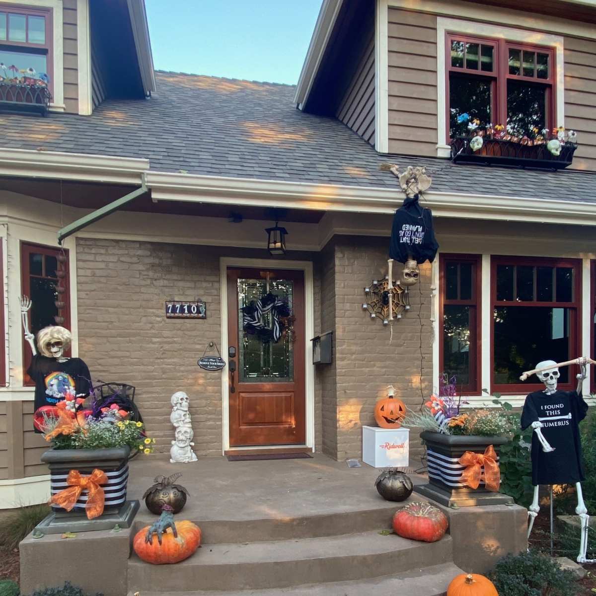 A house decorated for Halloween features a front porch with pumpkins, skeletons, and festive ornaments.