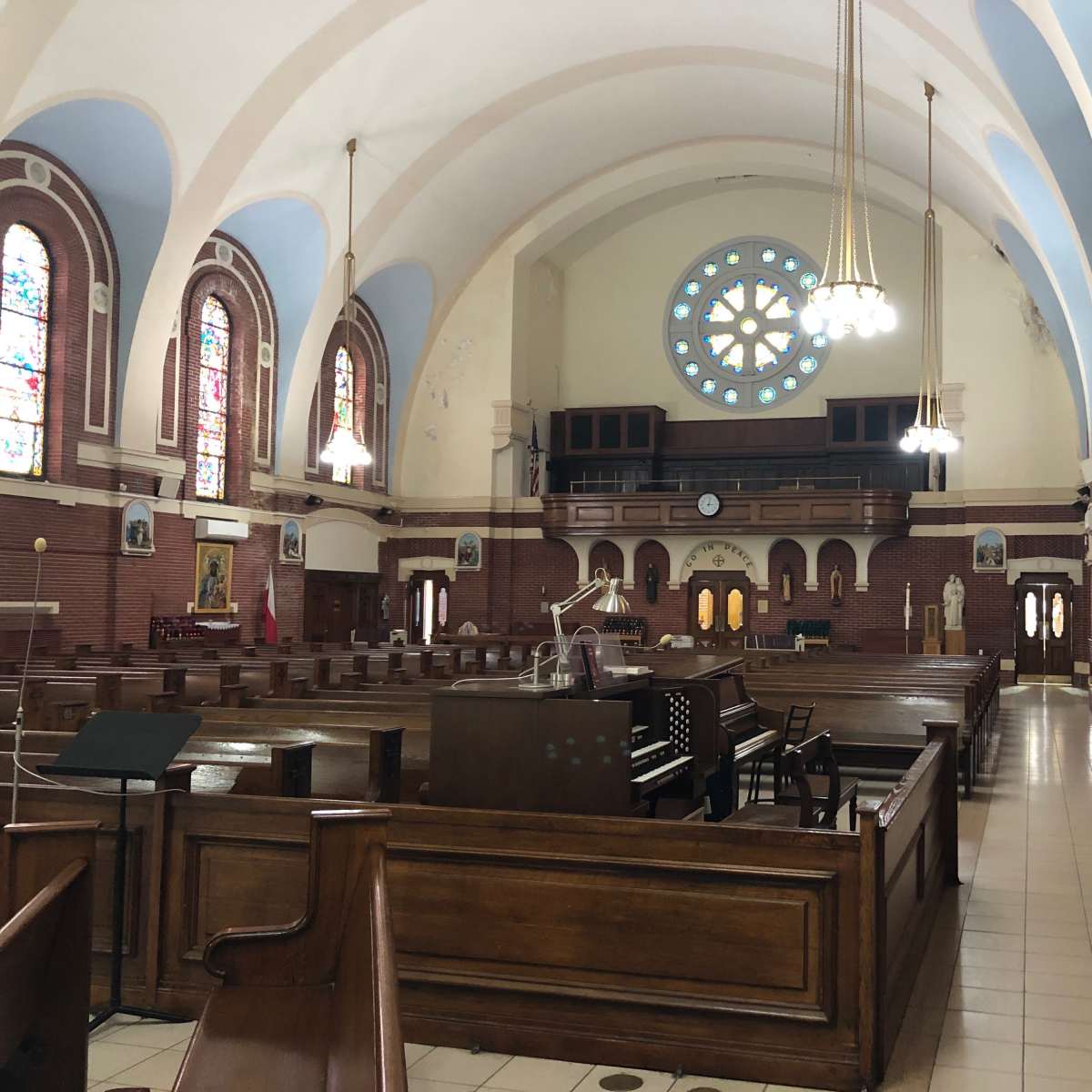 The interior of a church features wooden pews, a large stained glass window, and ornate chandeliers hanging from a high ceiling.