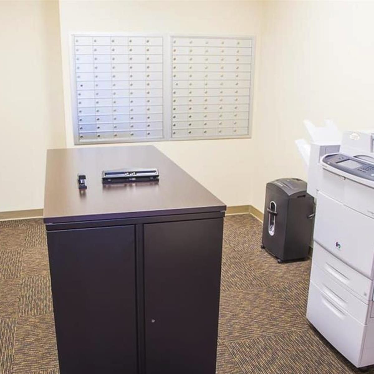 A small office space with a black cabinet, a photocopier, a microwave, and a mail sorting station against the wall.