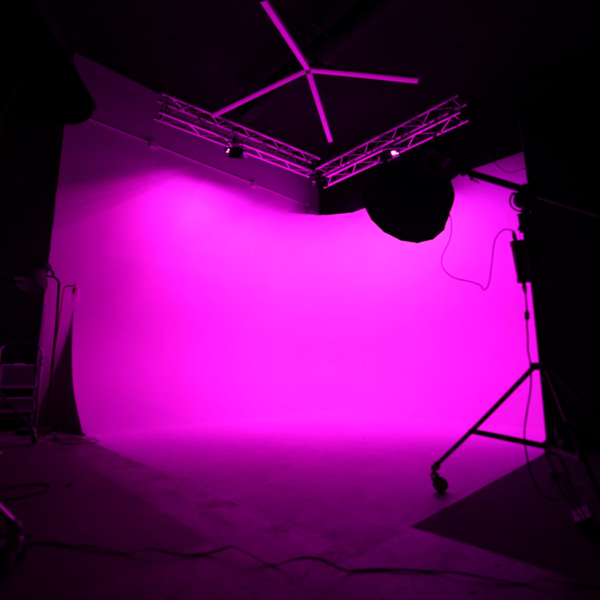 A photography studio with a bright pink backdrop and lighting equipment set up.