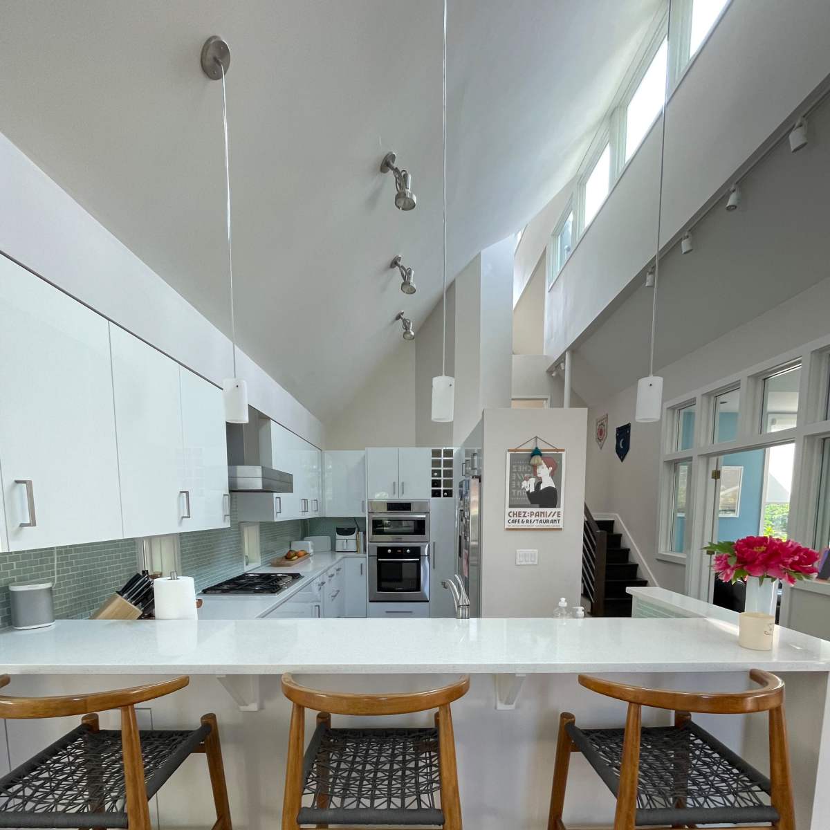 A modern kitchen with white cabinetry, stainless steel appliances, and three wooden bar stools arranged at a counter.