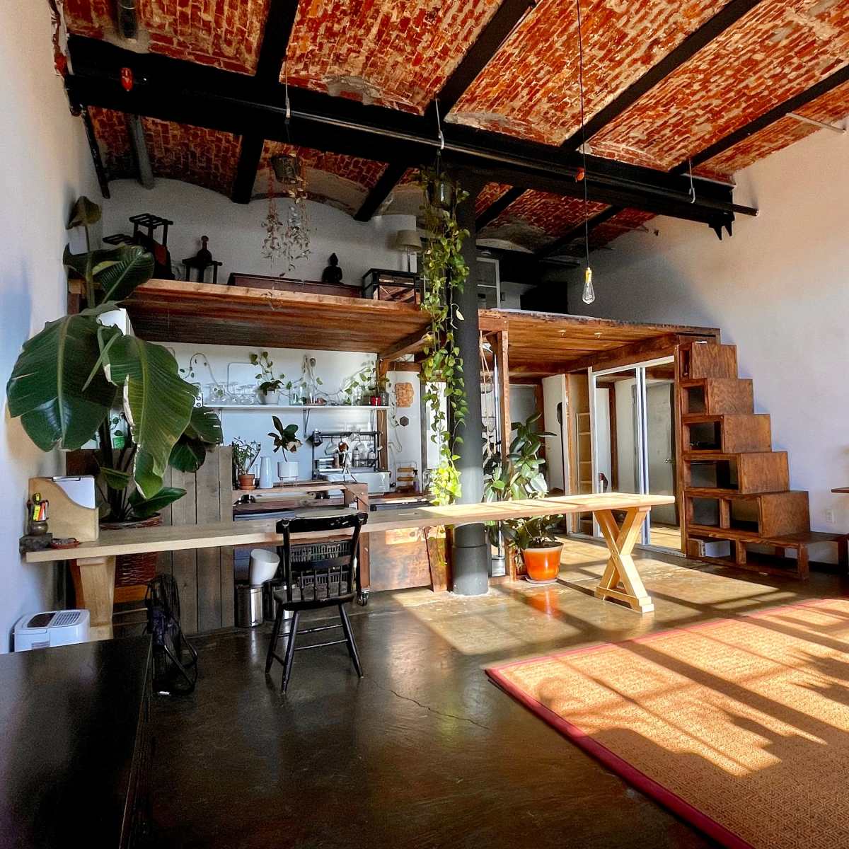 A spacious living area with a wooden loft, plants, and a mix of furniture, including a table, chairs, and a couch.