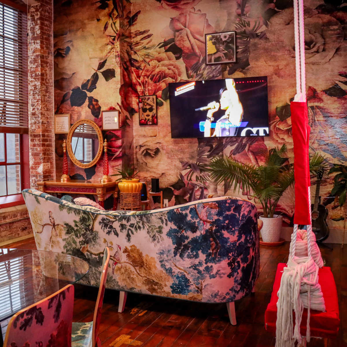 A vibrant living room featuring floral wallpaper, a patterned couch, a large television mounted on the wall, and a swing hanging from the ceiling.
