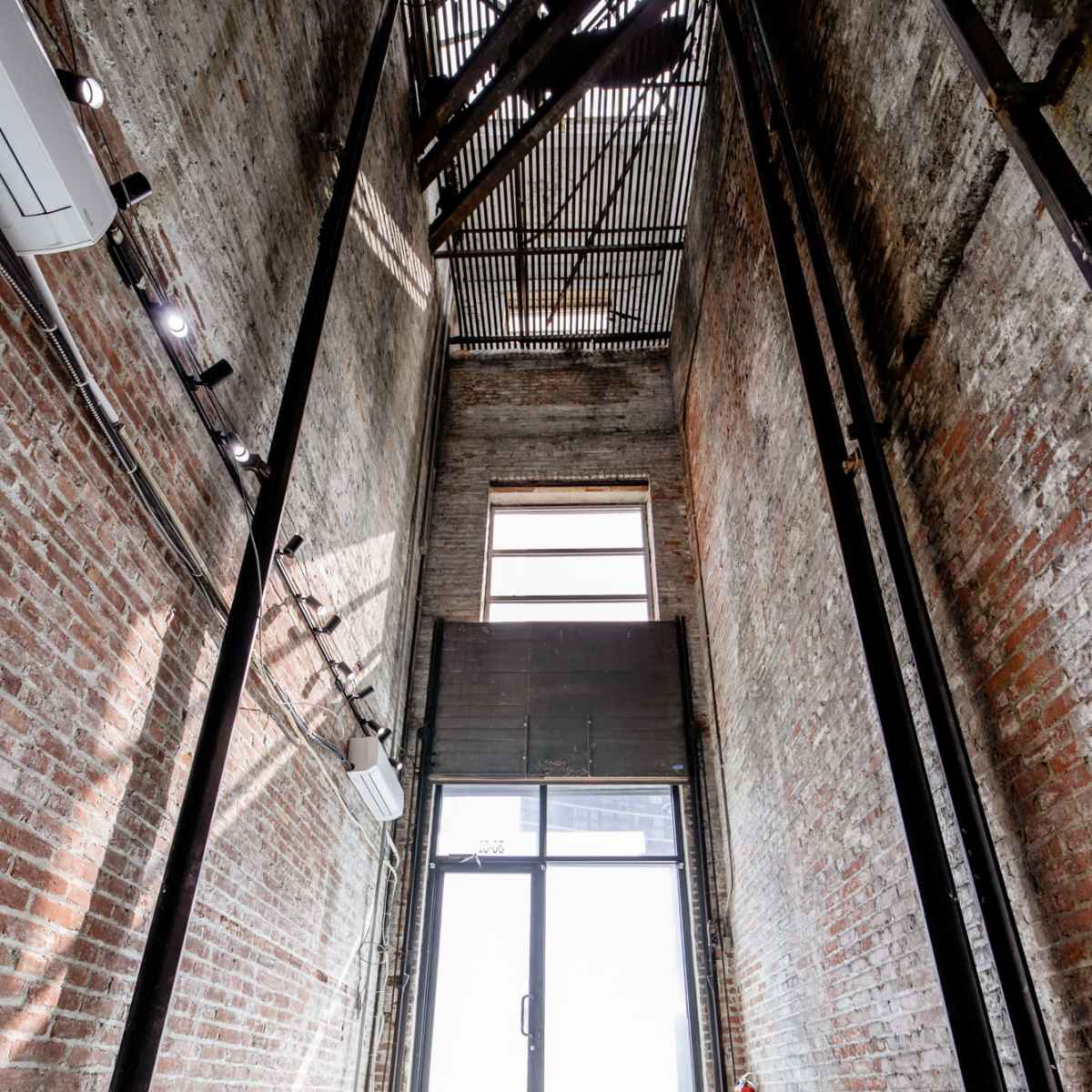 A tall, brick-walled interior space with large windows and a glass door at the end, illuminated by natural light.
