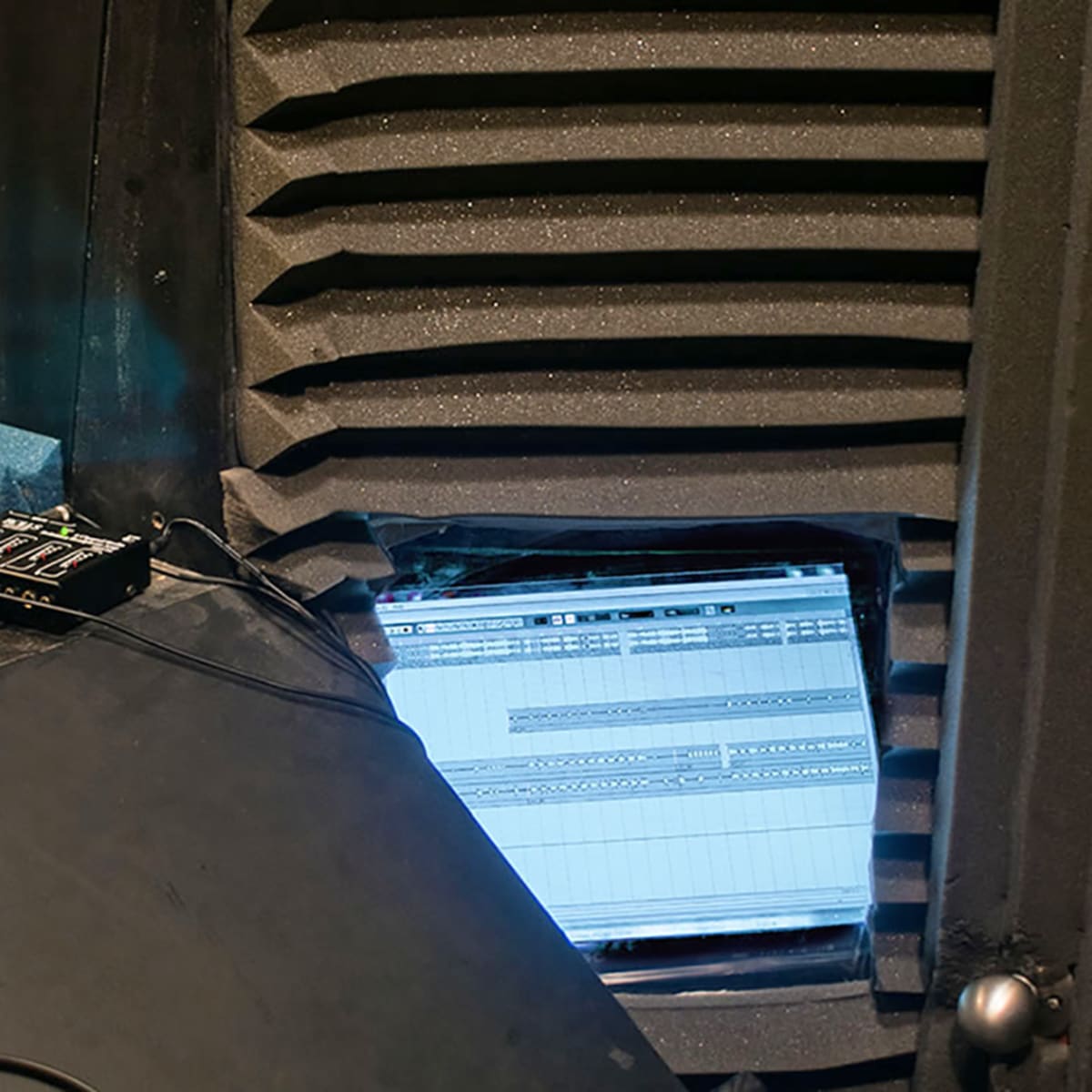 A recording studio with soundproofing panels, a computer screen displaying audio editing software, and a mixer connected to the setup.