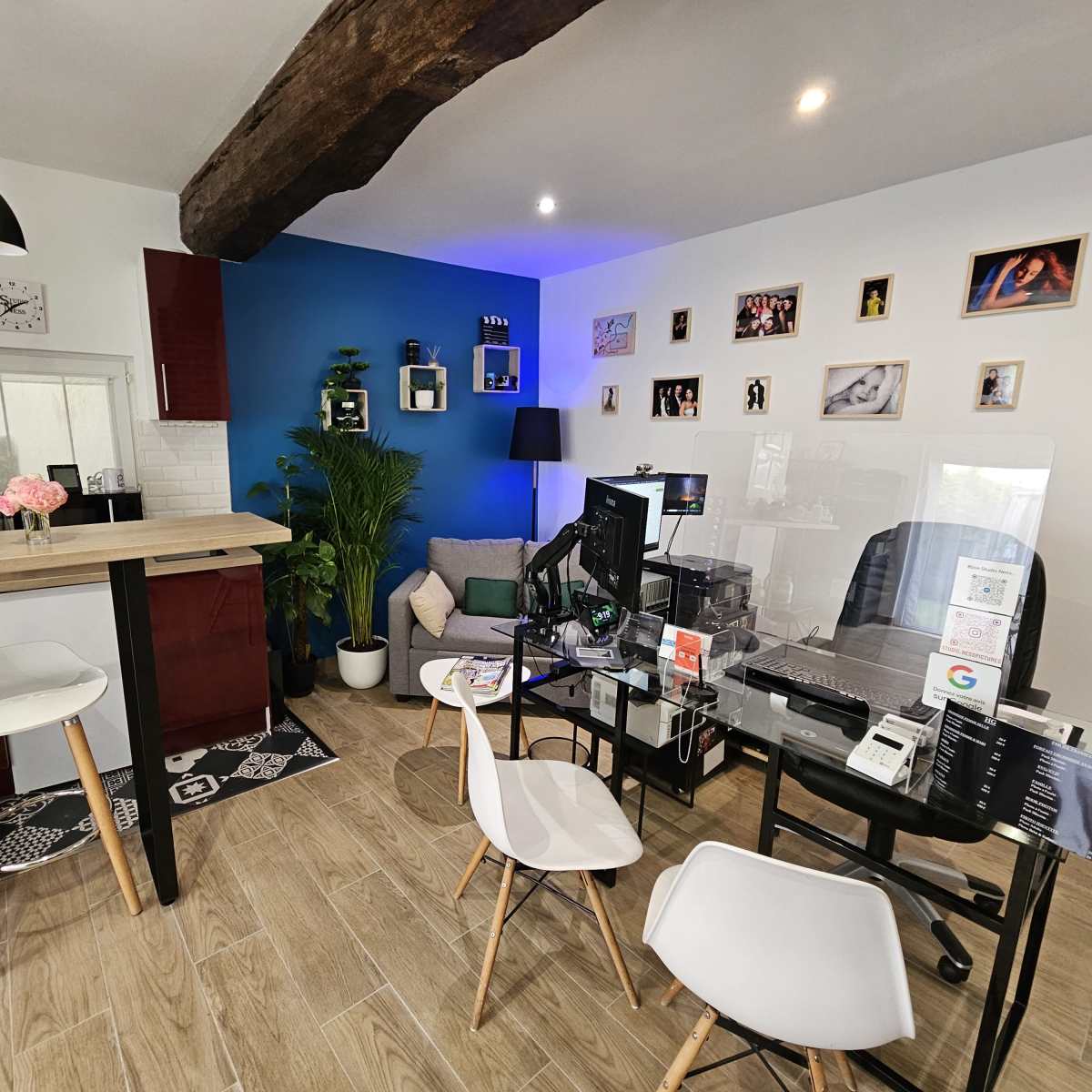 A modern workspace with a desk, computer, and chairs, set against a blue accent wall and decorated with framed photos and a plant.