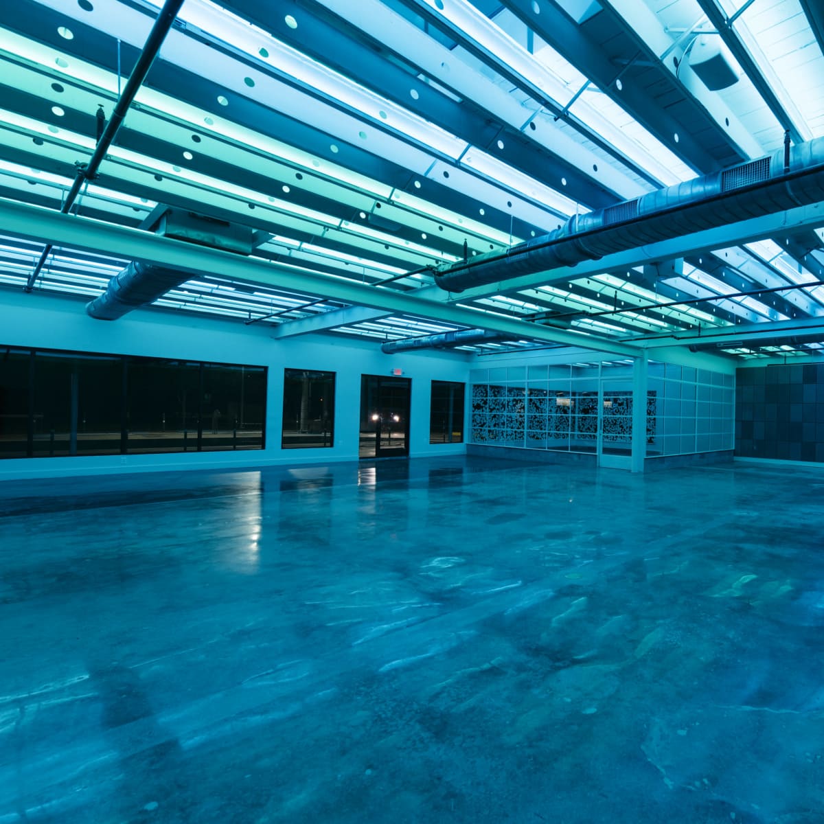 A large, empty room with polished concrete floors and overhead lights casting a blue-green glow.
