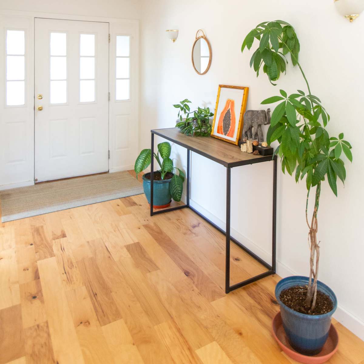 A hallway with a console table, two potted plants, and a mirror, leading to a set of double doors.