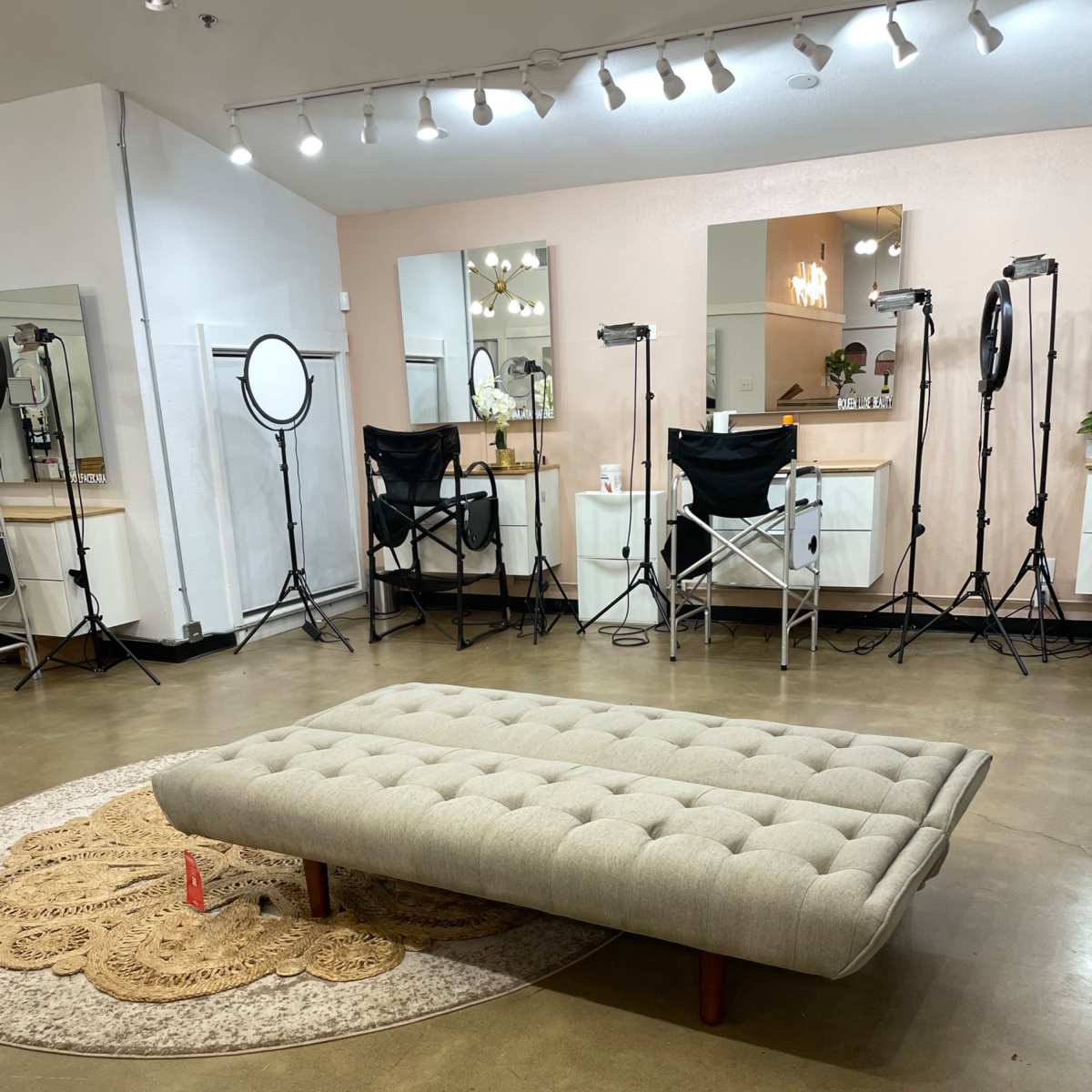 A spacious room with a light-colored floor, a large tufted sofa in the center, and several mirrors and lighting equipment arranged around the walls.