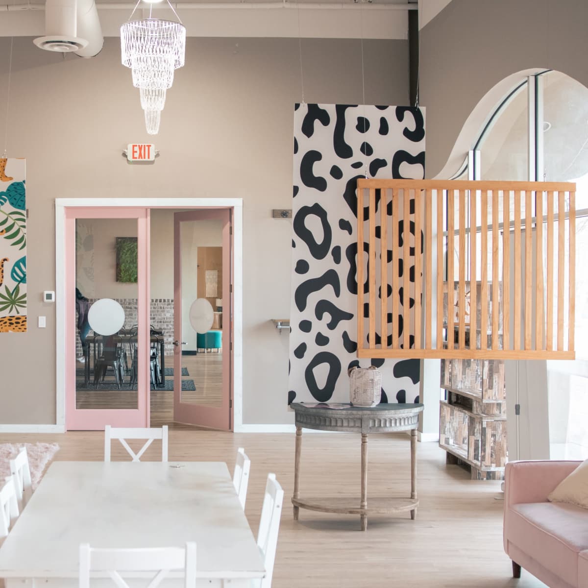 A brightly lit interior space featuring colorful wall murals, wooden partitions, and a dining table surrounded by chairs.