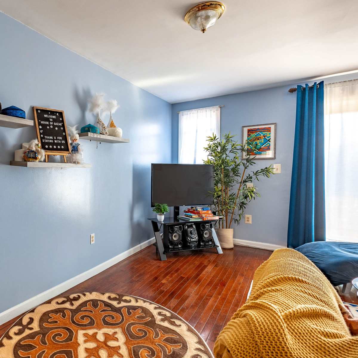 A living room with a blue accent wall, two decorative shelves, a television on a stand, and a couch with a patterned rug.