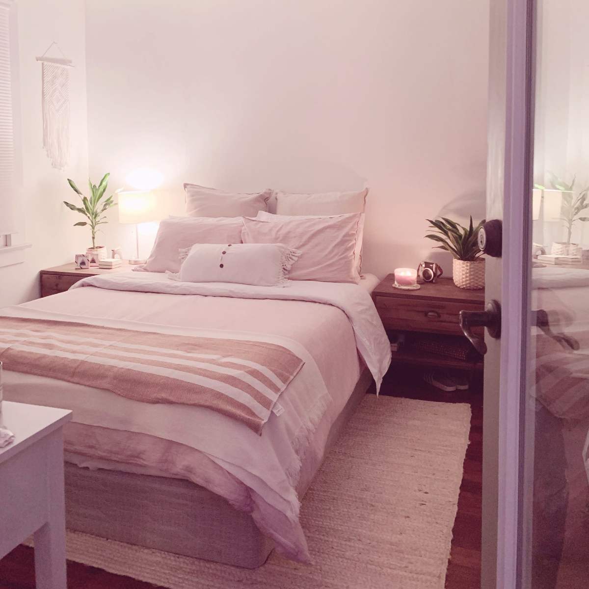 A cozy bedroom with a neatly made bed, bedside tables with lamps, and potted plants.