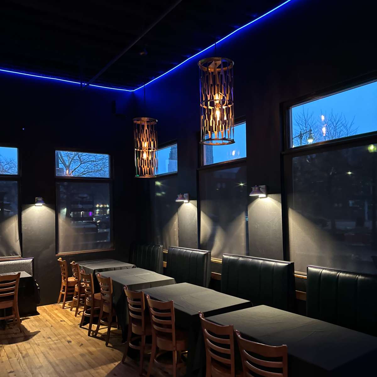 The interior of a restaurant features wooden tables with black tablecloths, illuminated by pendant lights and blue LED accents along the ceiling.