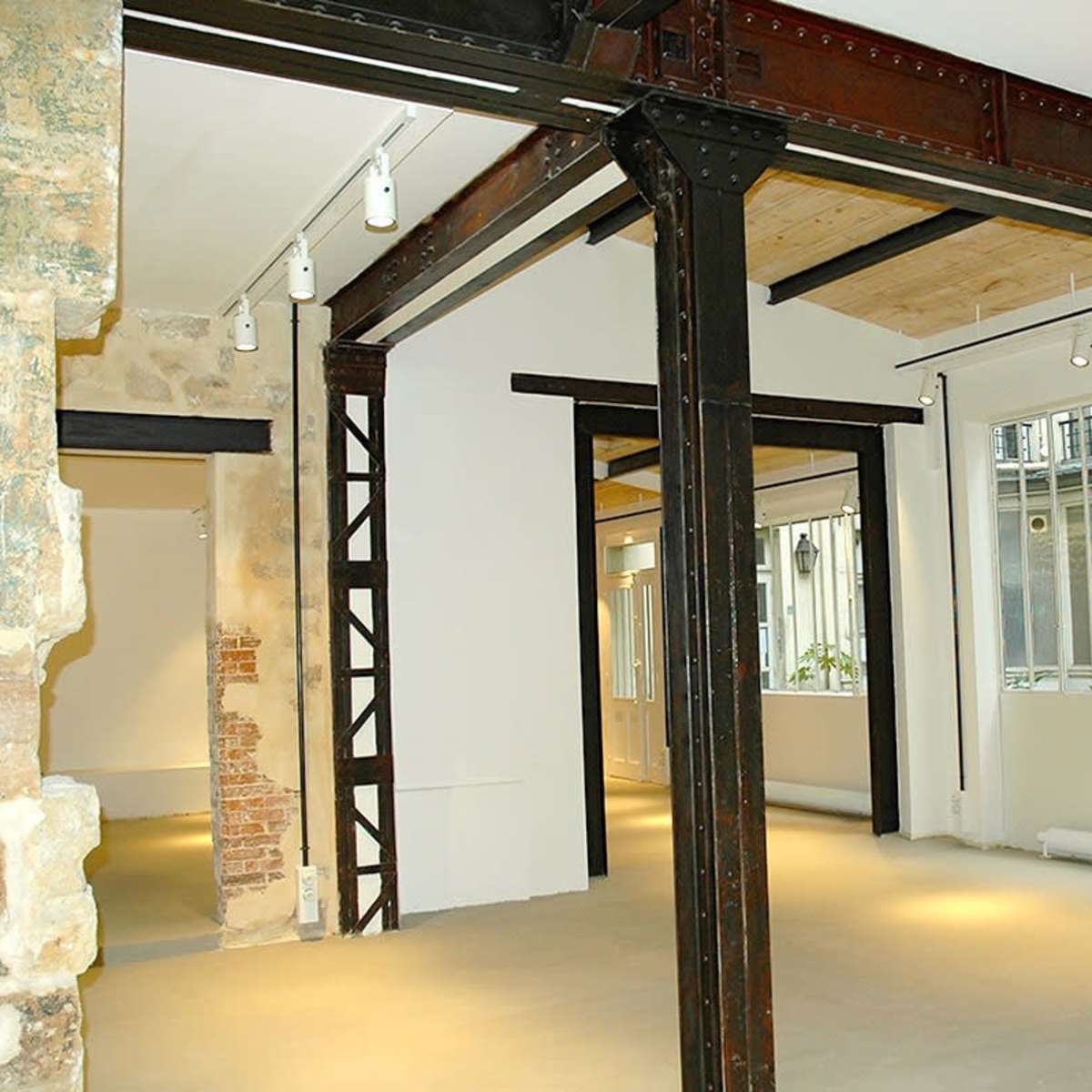 An interior space featuring exposed metal beams, concrete flooring, and large windows allowing natural light to enter.