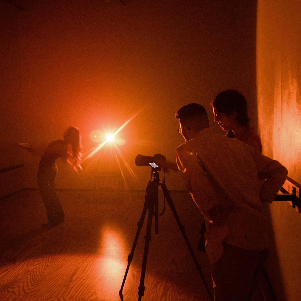 A dancer performs in a dimly lit studio while two photographers observe and prepare their equipment.