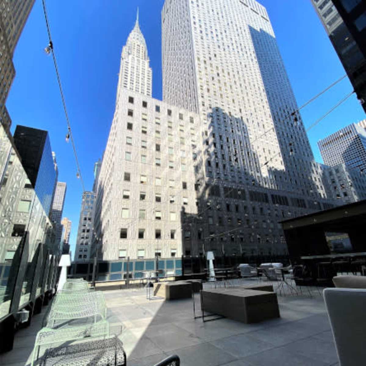 A modern terrace with seating and a view of tall skyscrapers, including the iconic Empire State Building in the background against a clear blue sky.
