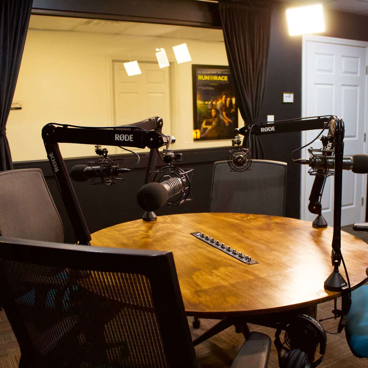 A recording studio equipped with two microphone stands, a round wooden table, and chairs arranged around it.