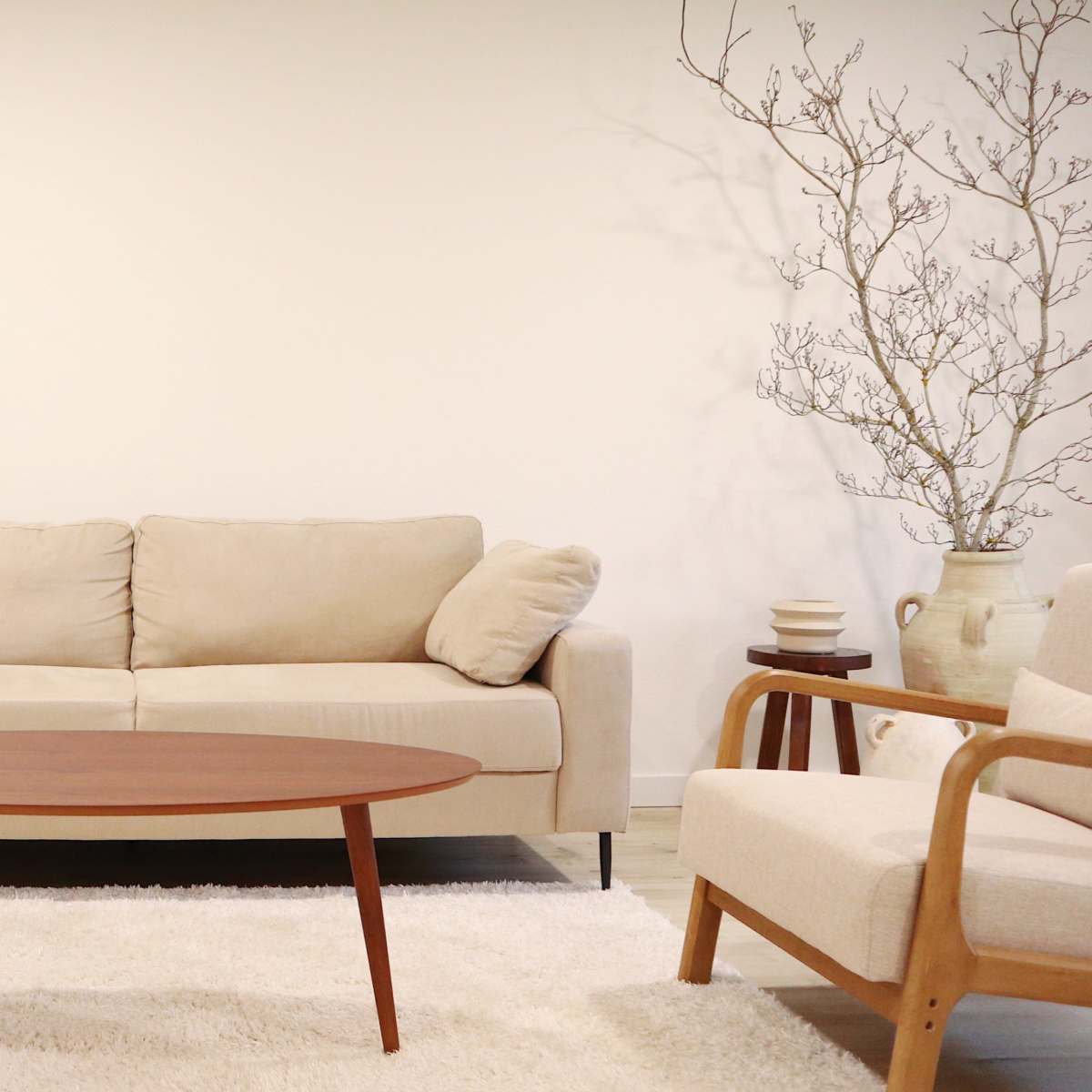 A modern living room with a beige sofa, two armchairs, a round wooden coffee table, and a tall mirror against a white wall.