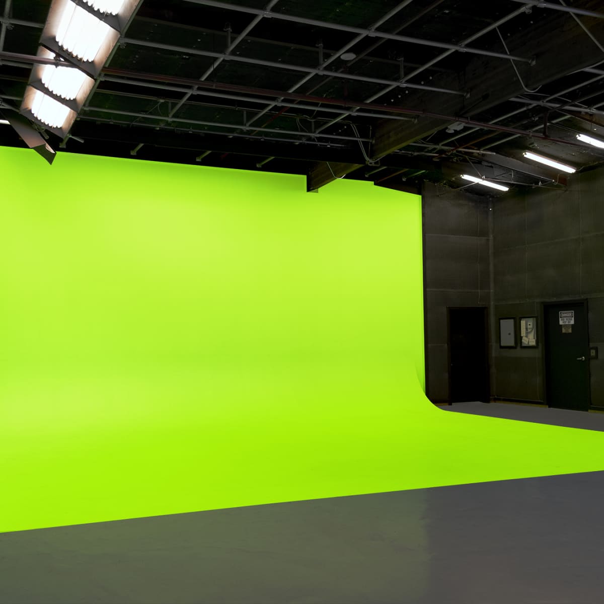 A spacious studio with a bright green screen background and gray flooring.