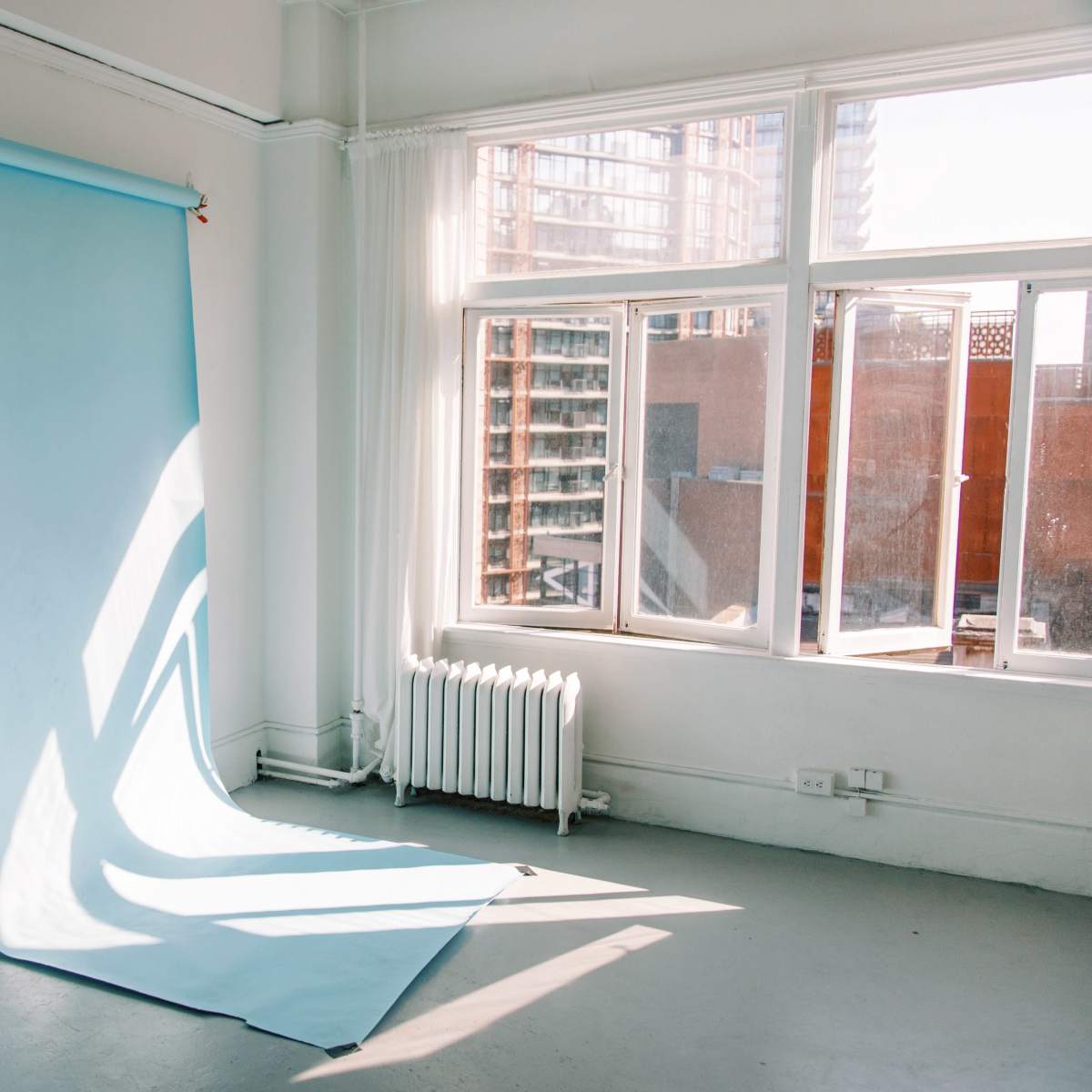 A light blue backdrop against a white wall in a sunlit room with large windows and a mirror.