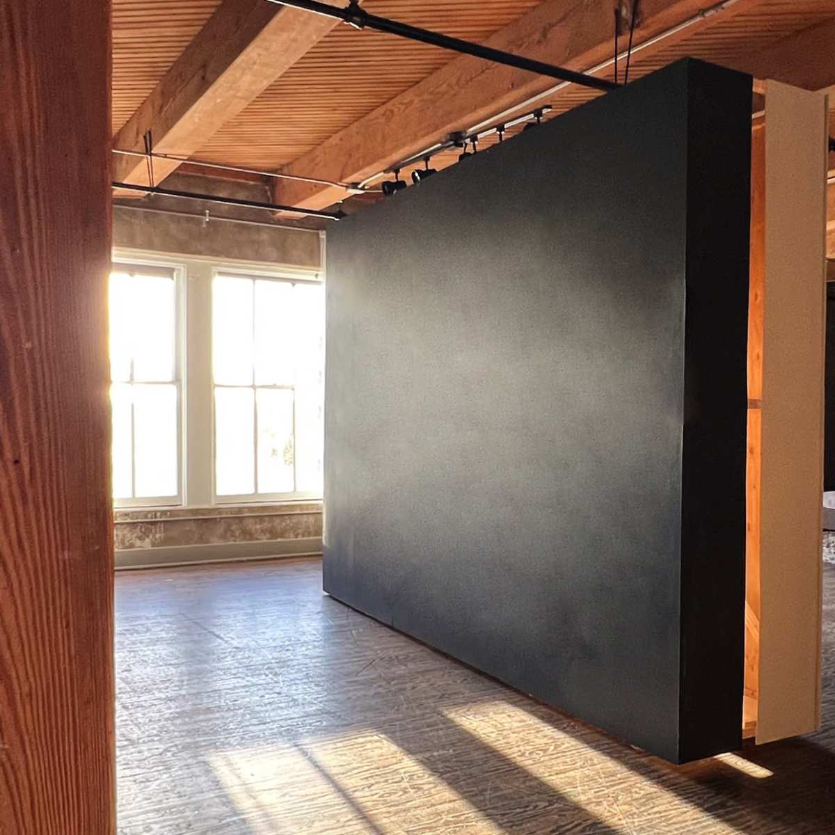 An open-concept interior space with exposed wooden beams, featuring a large black partition separating areas with natural light coming through windows.