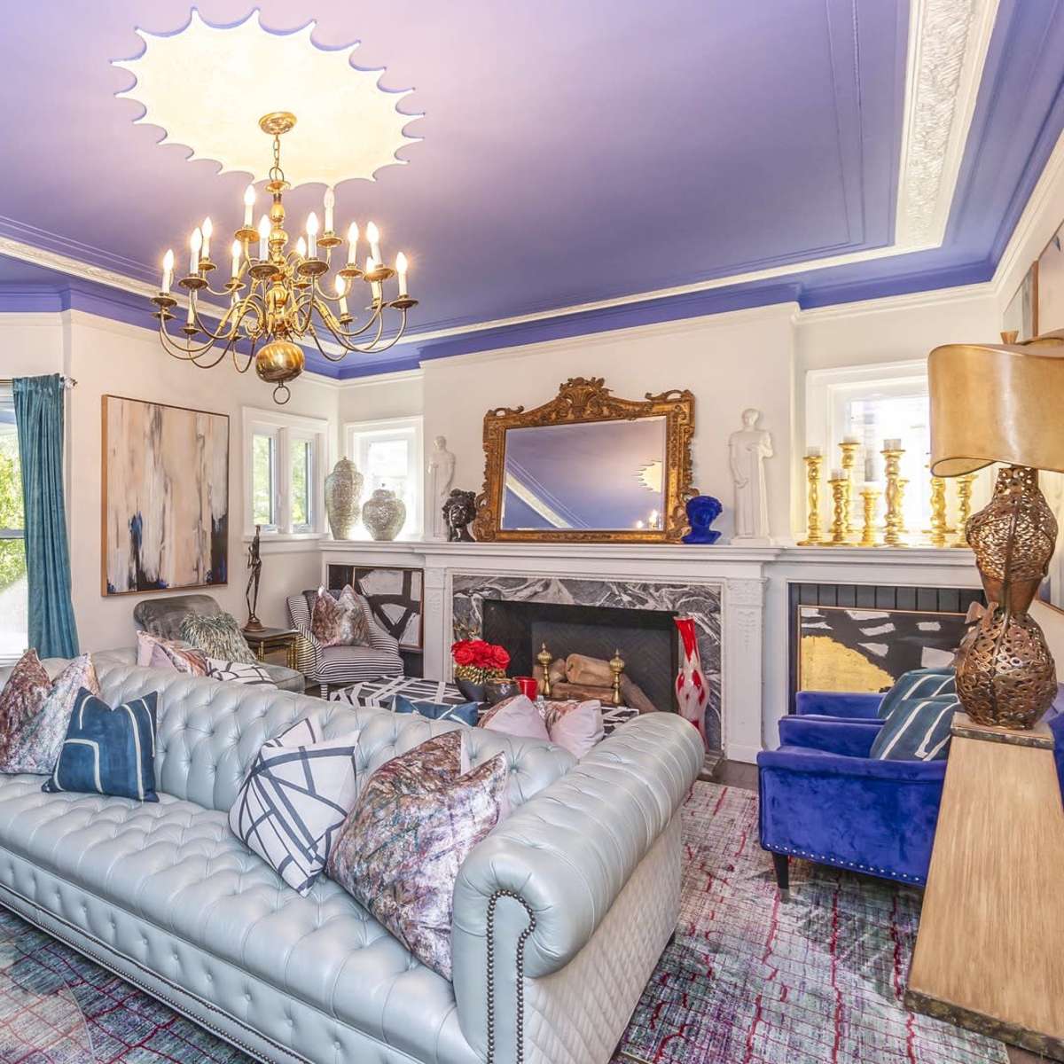 The living room features a blue ceiling, a chandelier, a light-colored sofa with decorative cushions, and various pieces of artwork and decor.