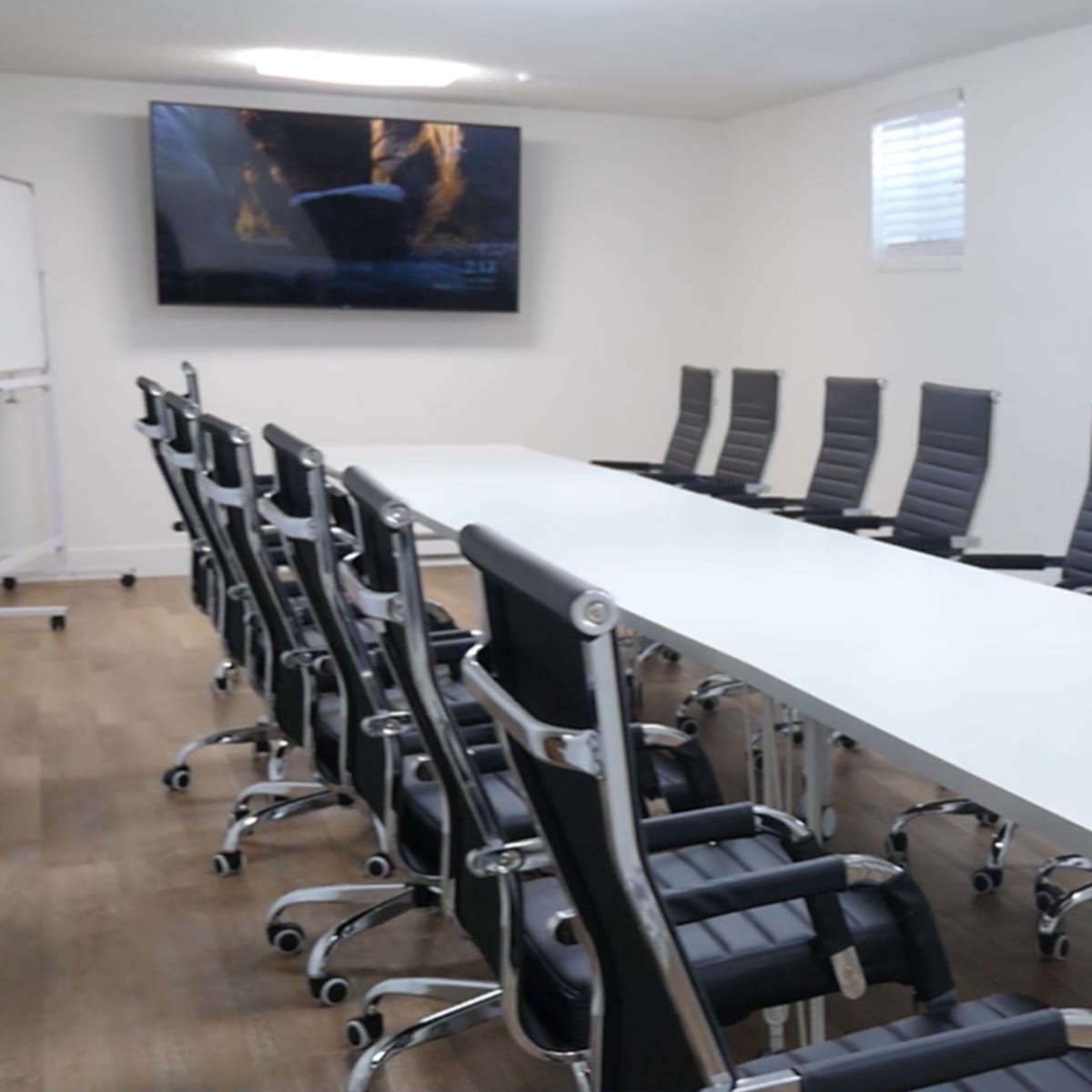 A long white conference table is set with black ergonomic chairs in a well-lit meeting room.