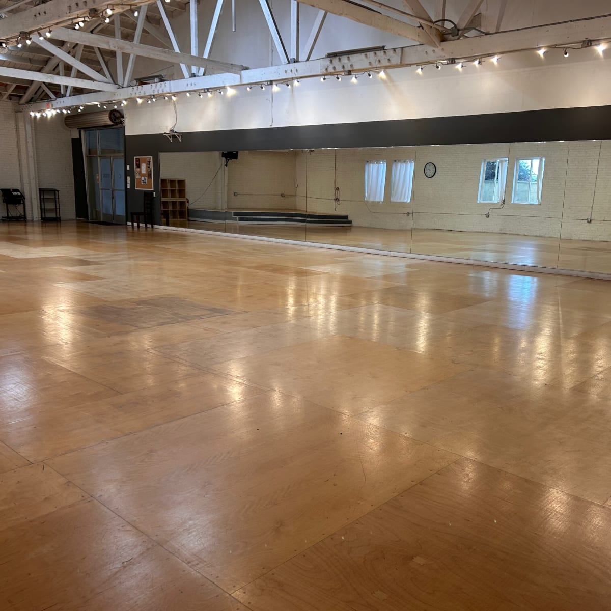 A spacious dance studio with polished wooden floors, large mirrors along one wall, and natural light coming through windows.