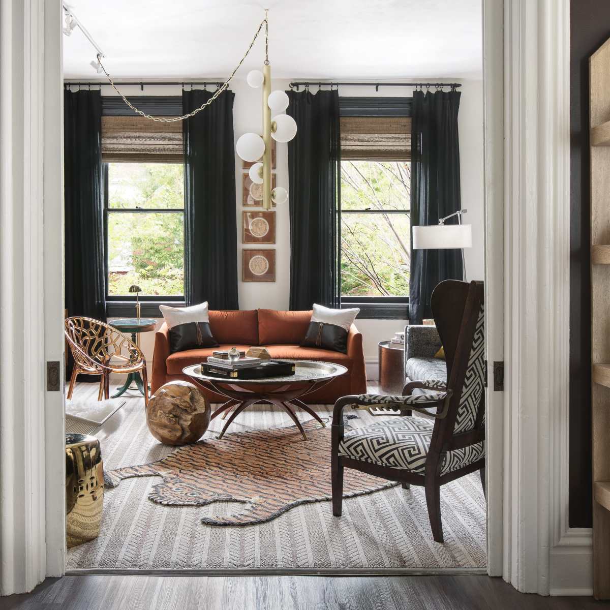 A cozy living room features a circular coffee table surrounded by an orange sofa, with bookshelves and large windows framing the space.