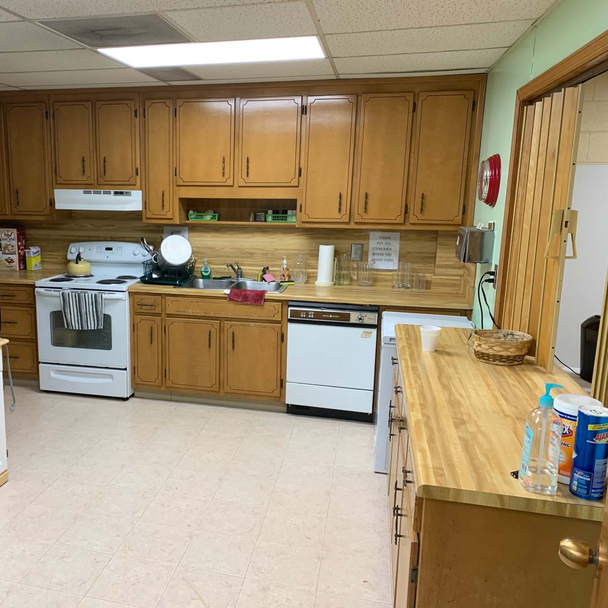 A kitchen with wooden cabinets, a white stove and dishwasher, a black refrigerator, and a countertop with various kitchen items.