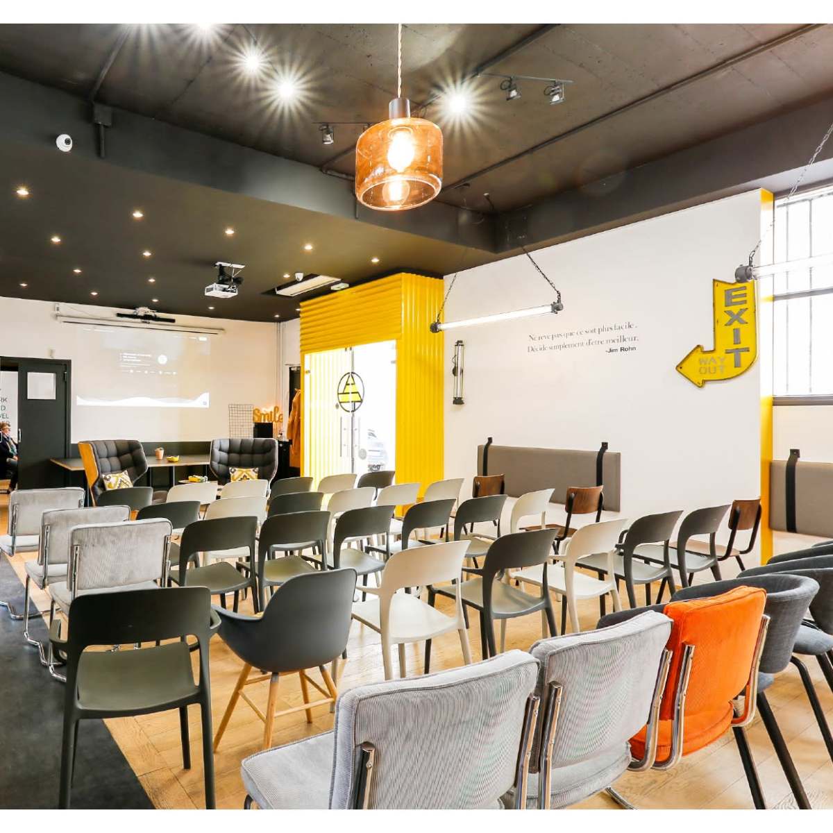 A modern workshop space features rows of chairs facing a presentation area, with a coffee bar and bright yellow accents on the walls.