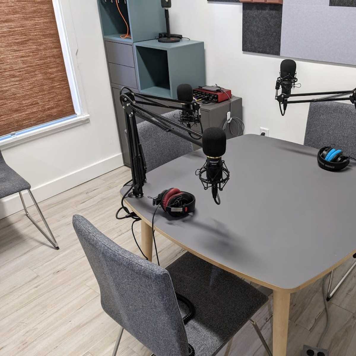A small recording studio features a gray table with three microphones on adjustable arms and two chairs.