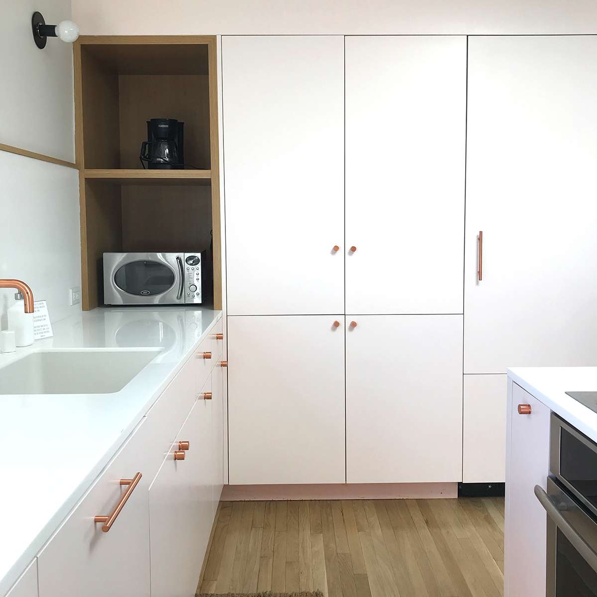 A modern kitchen with white cabinets, a built-in microwave, and a coffee maker on a shelf.