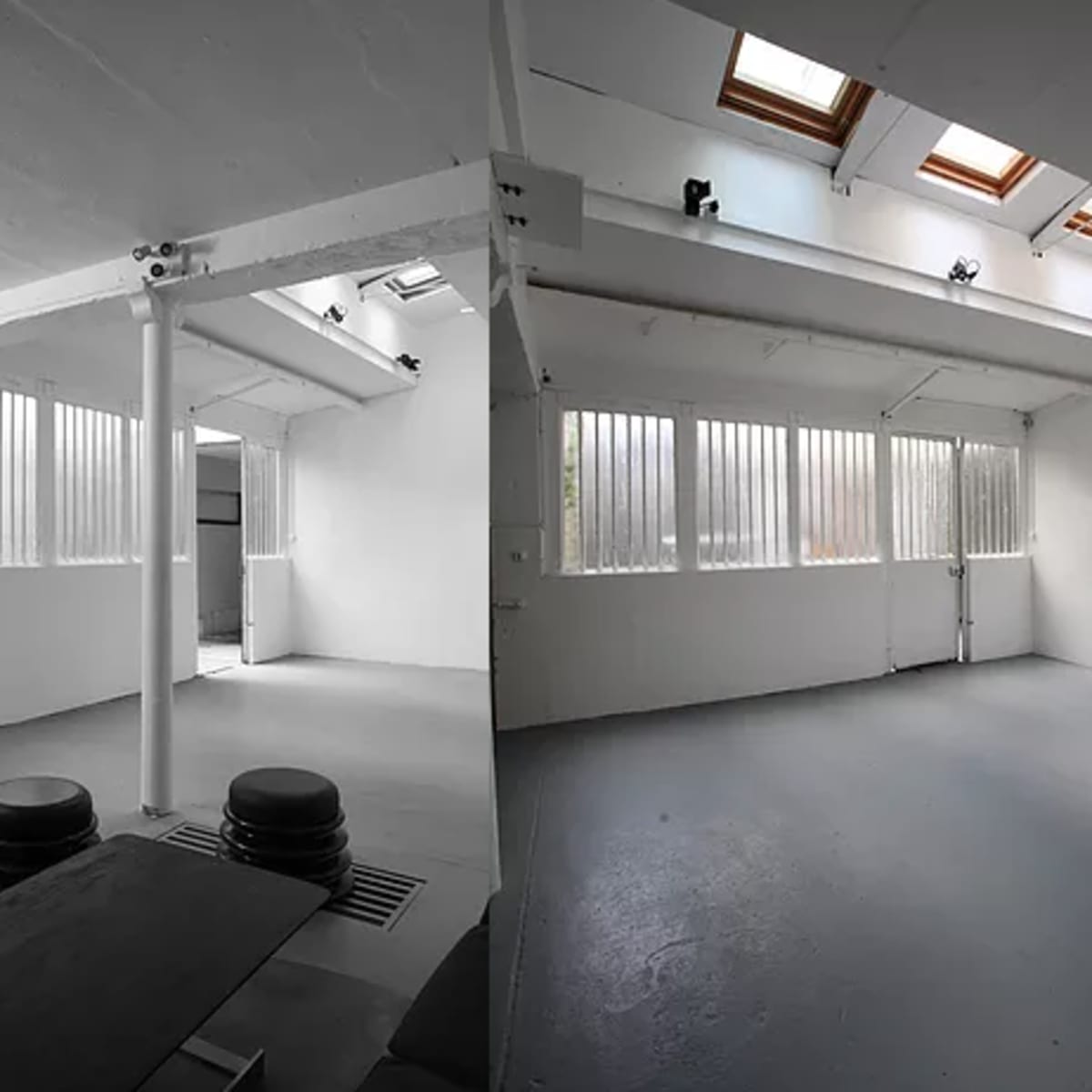A spacious, bright studio with high ceilings, skylights, and large windows, featuring minimal furnishings and a gray floor.