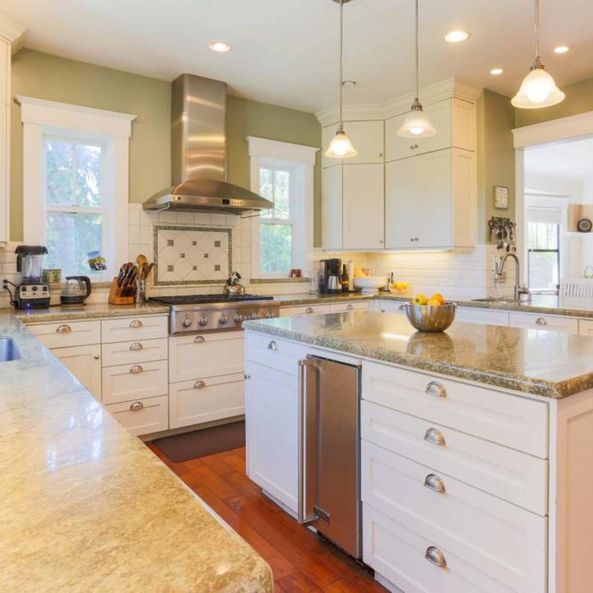 A spacious kitchen features white cabinetry, a large island with a granite countertop, stainless steel appliances, and hardwood floors.