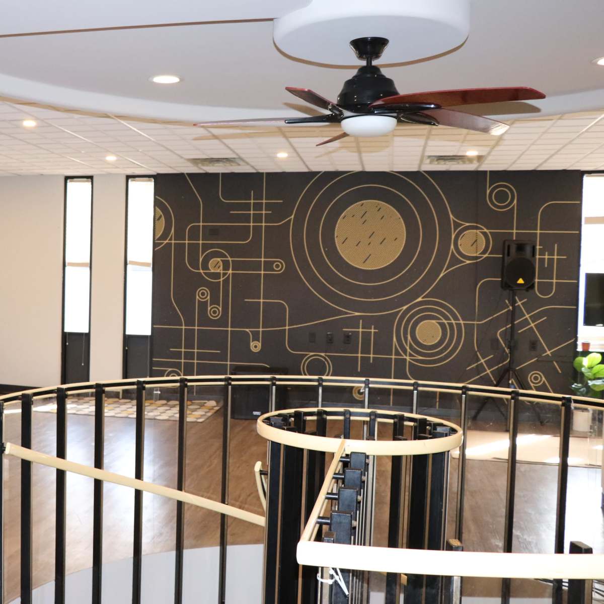 A large, modern room with wooden flooring, a circular staircase, and a geometric patterned accent wall.