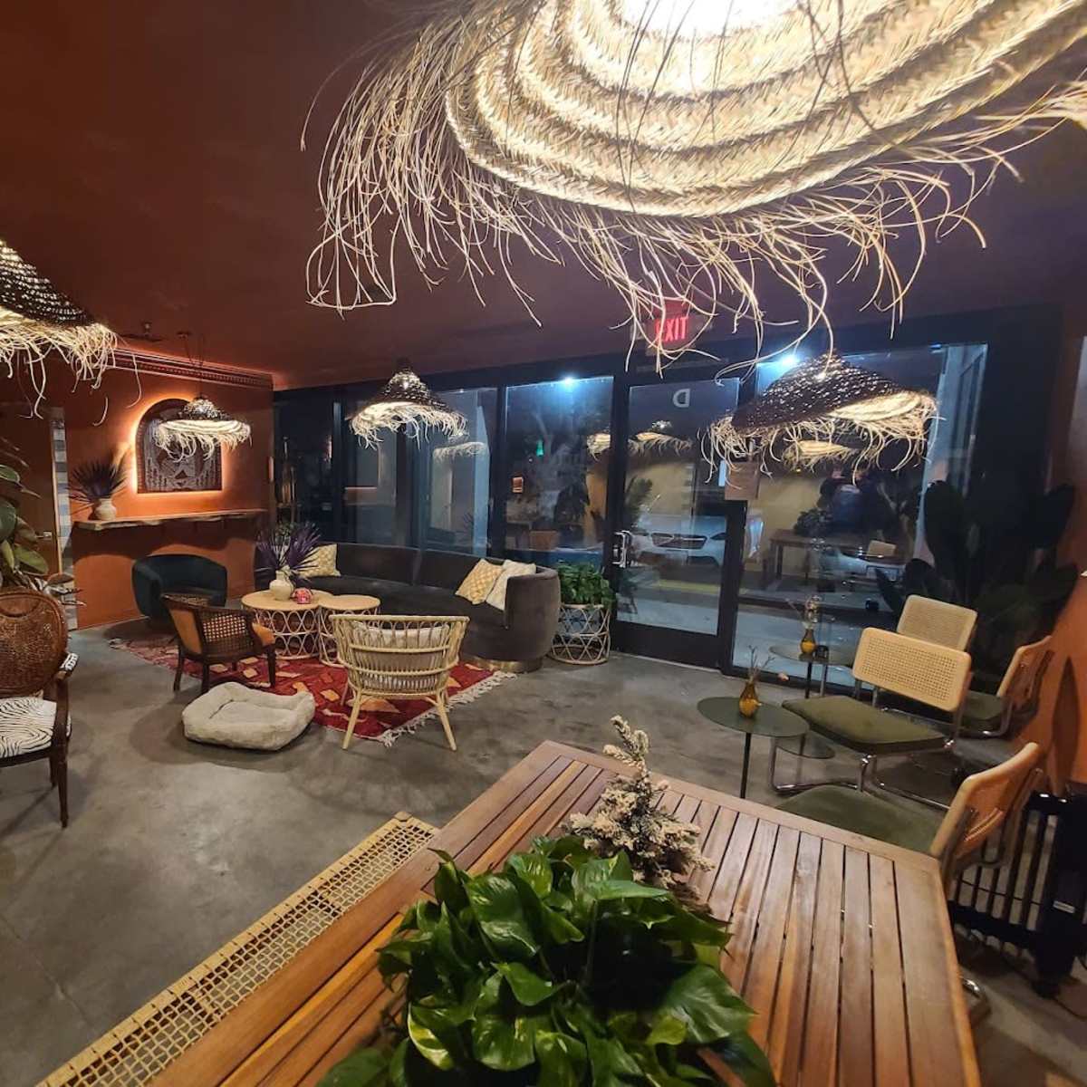 A cozy indoor lounge area with various seating arrangements, decorative plants, and unique woven light fixtures.