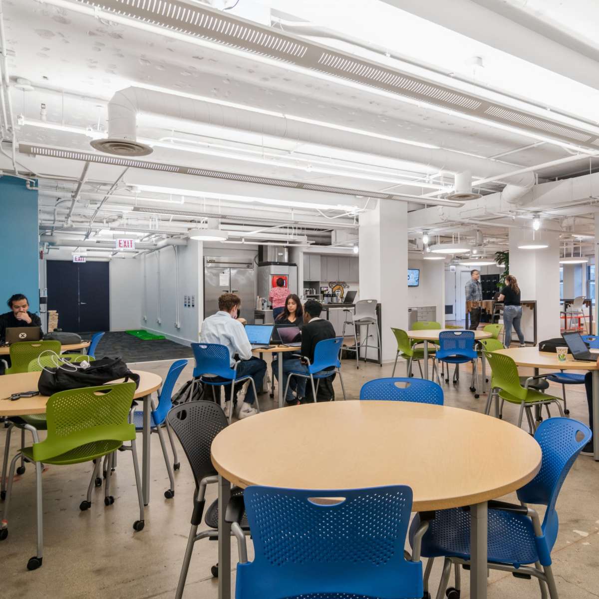 A modern office space with several round tables, people working on laptops, and open areas featuring creative design elements.